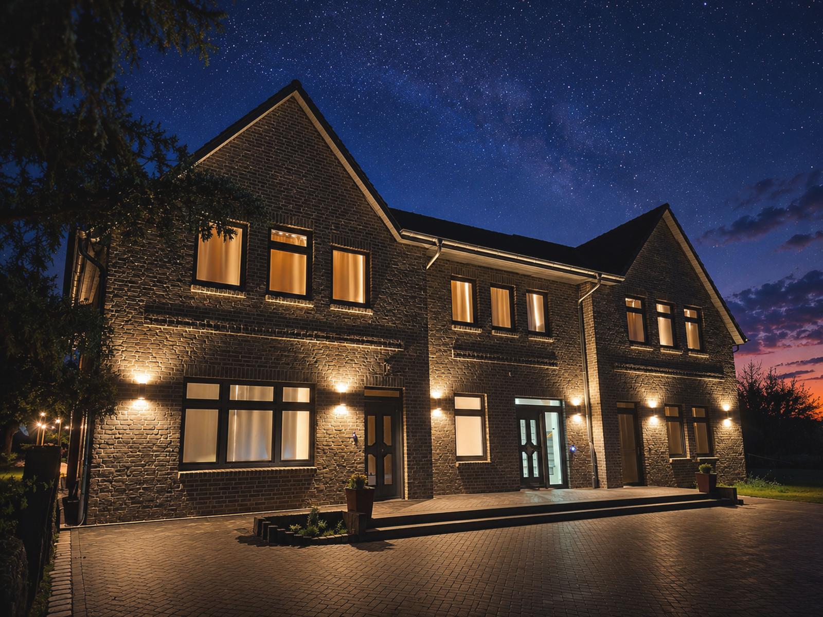 Haus mit Steinmauer, beleuchteten Fenstern und Sternenhimmel bei Nacht.