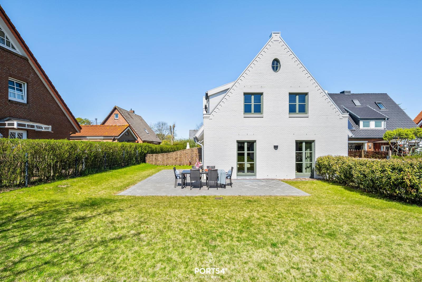 White villa with garden and terrace. Table and chairs on paved area.