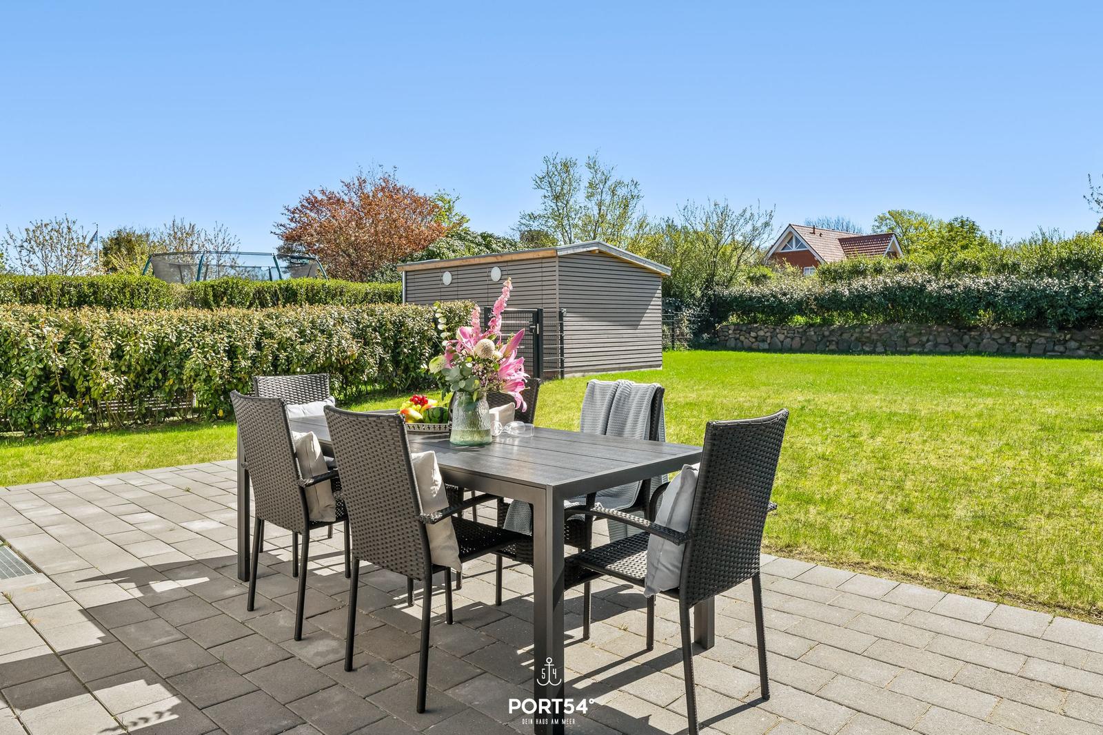 Patio with table and chairs, surrounded by lawn and hedge.