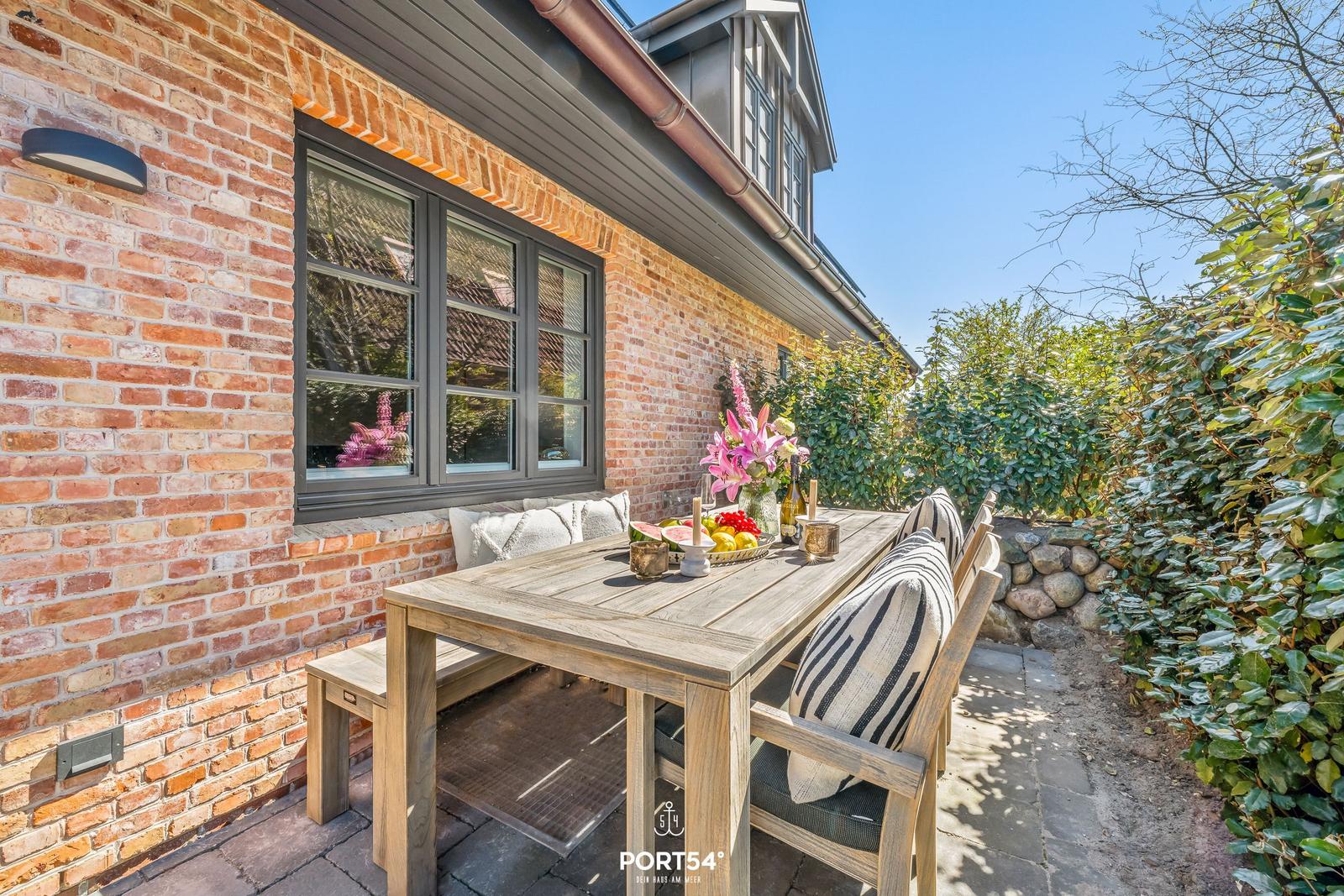 Terrace with wooden table, chairs, and flowers in front of brick house