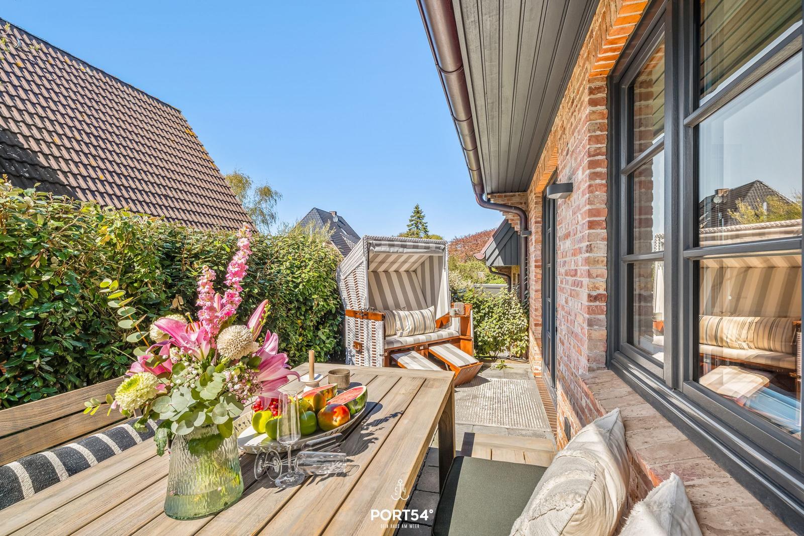 Terrace with wooden table, flowers, and lounge chair in front of brick house