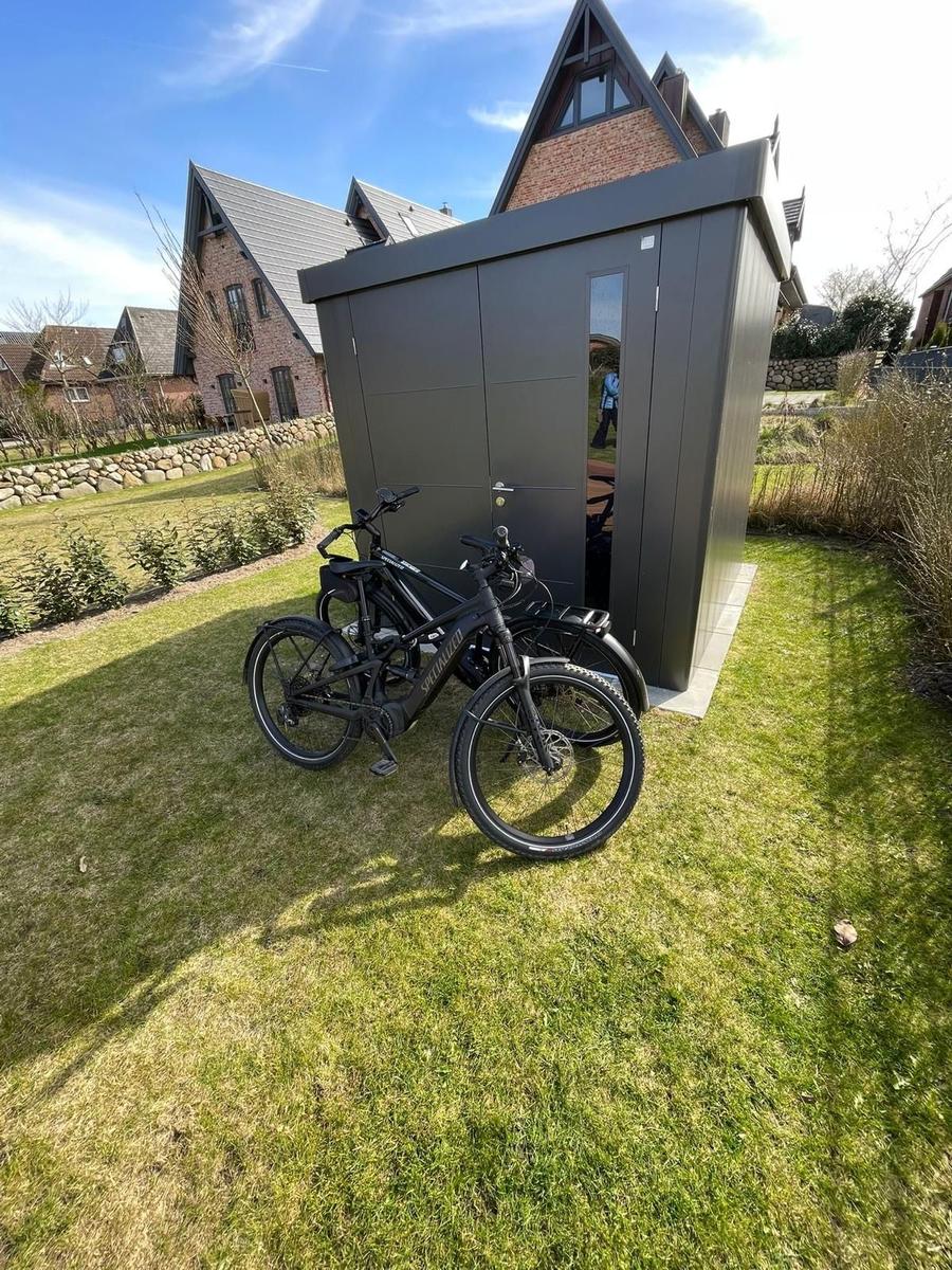 Two black bicycles stand in front of a gray shed in the garden.