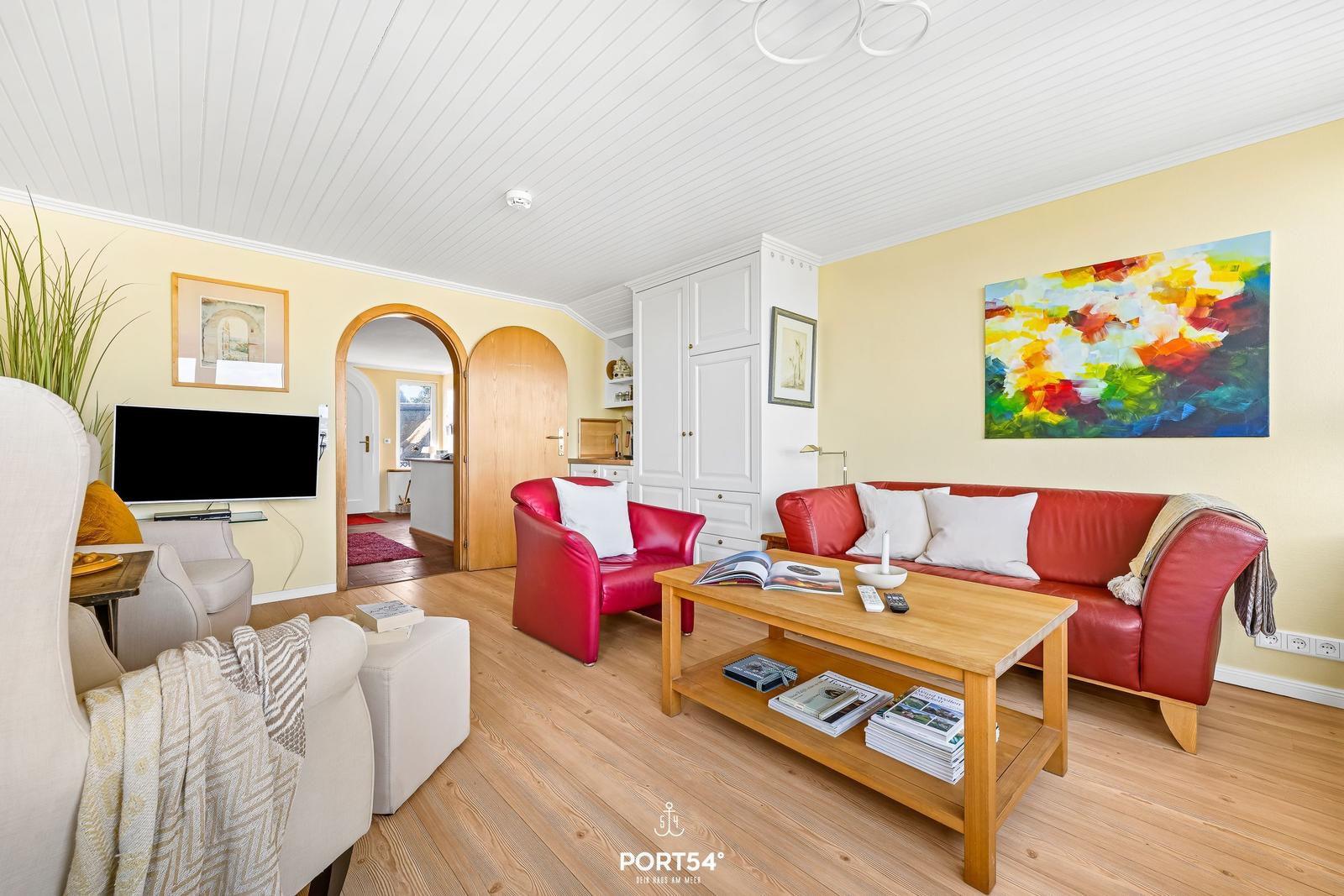 Living room with red sofa, wooden table, and TV on the wall.