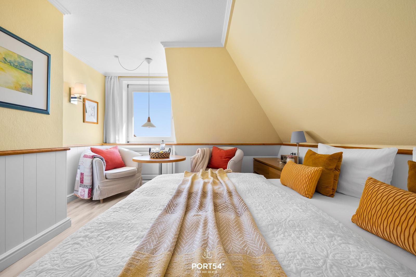 Bedroom with sloped ceiling, bed, armchairs, and window.
