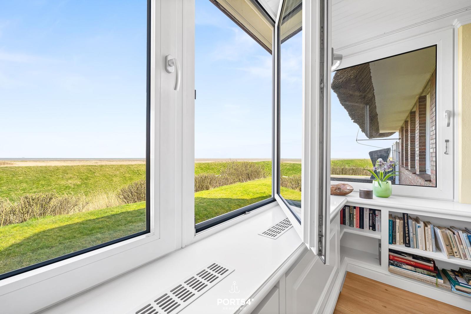 Wide view through large window onto green fields and sky.