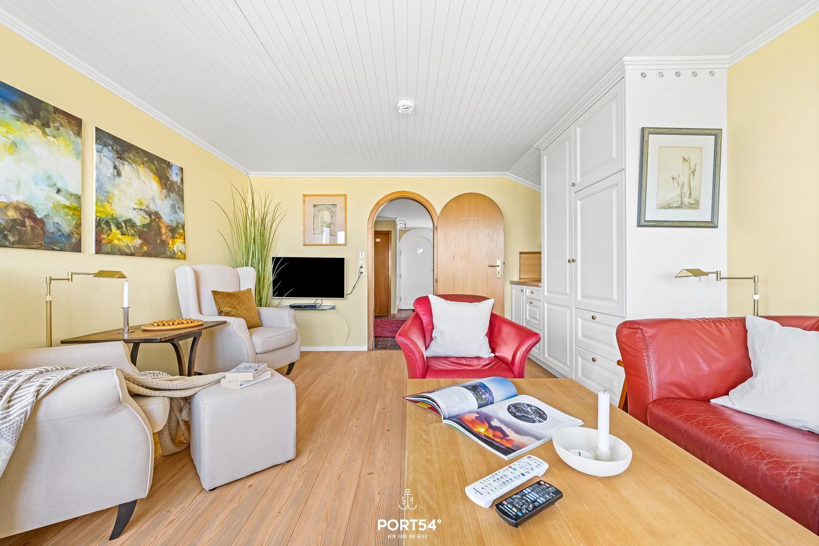 Living room with red sofa, white armchairs, and wooden floor.