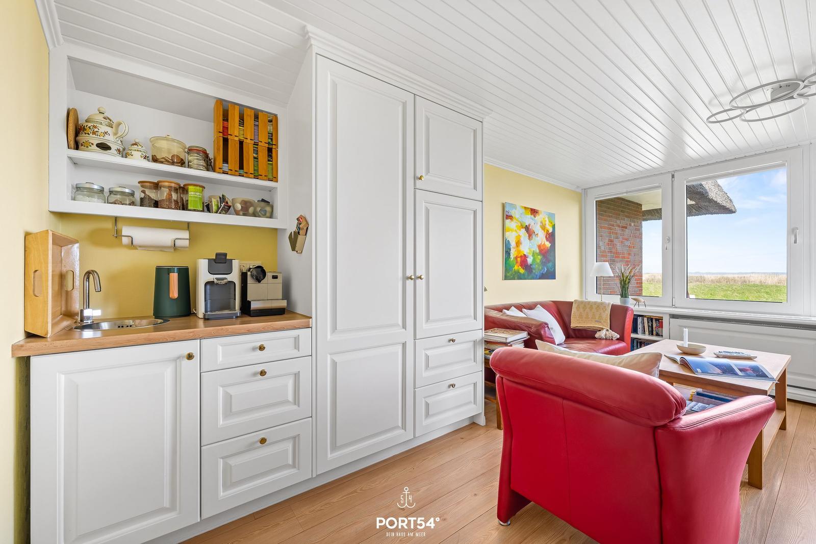 Living area with red sofa, kitchenette, and view of the field.