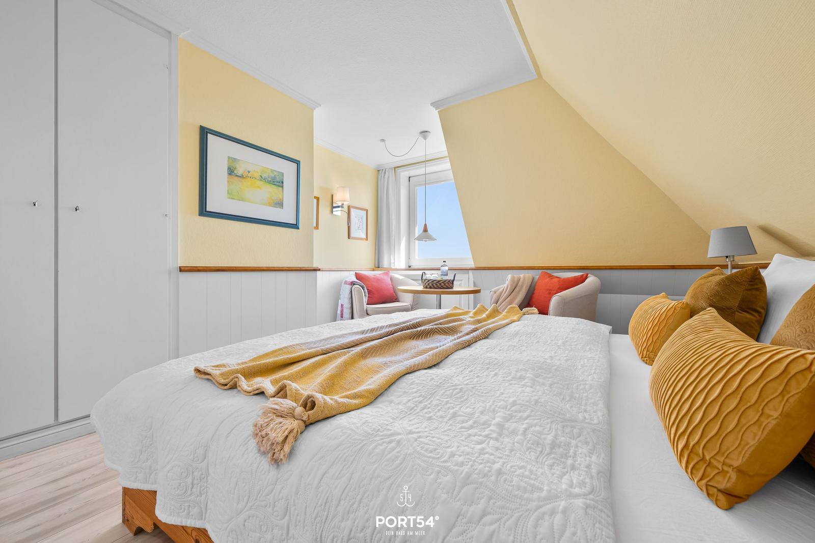 Bedroom with sloped ceiling, bed with pillows and wall art.
