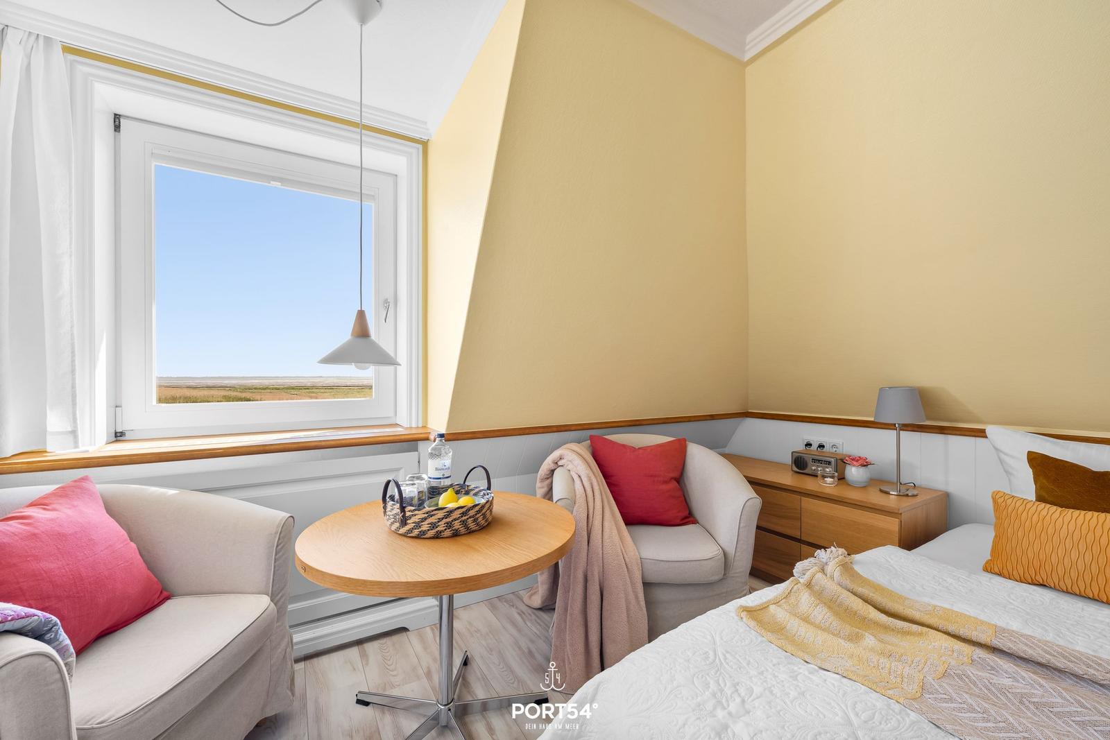 Bedroom with field view, two armchairs, table, and bed.