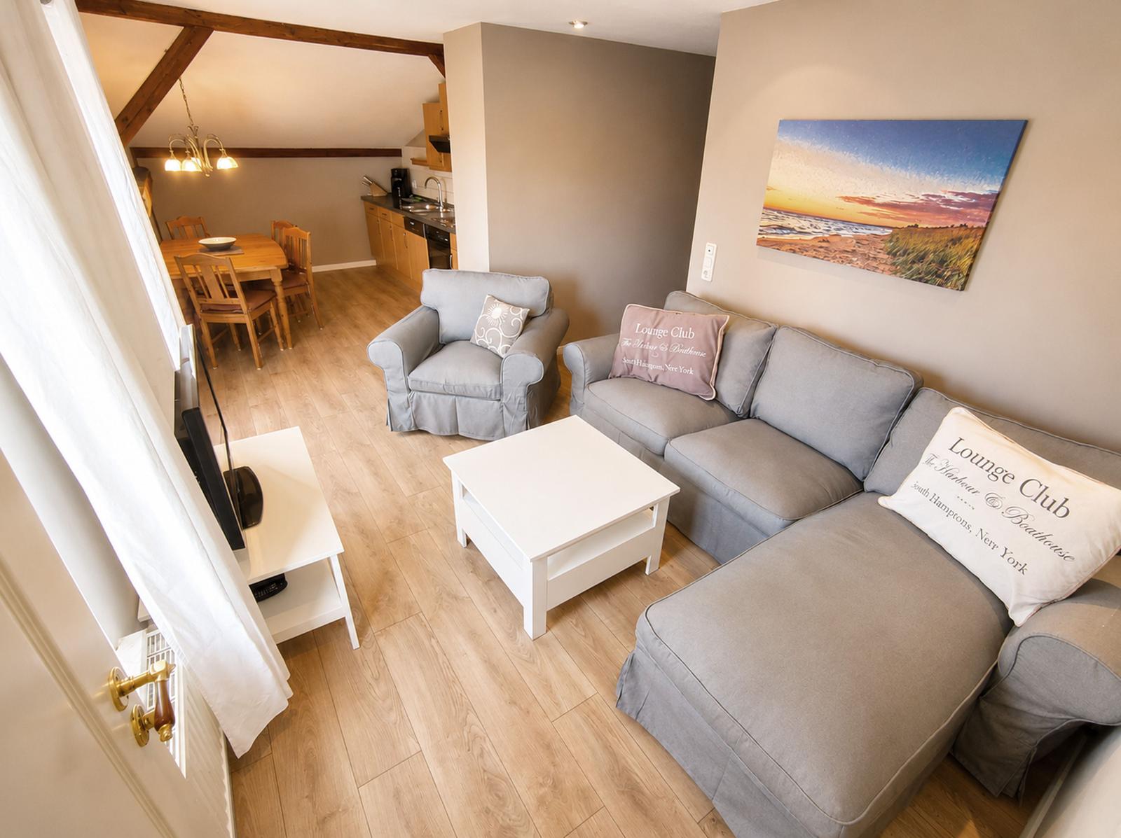 Wohnzimmer mit grauem Sofa, weißem Tisch und Küchenbereich im Hintergrund.