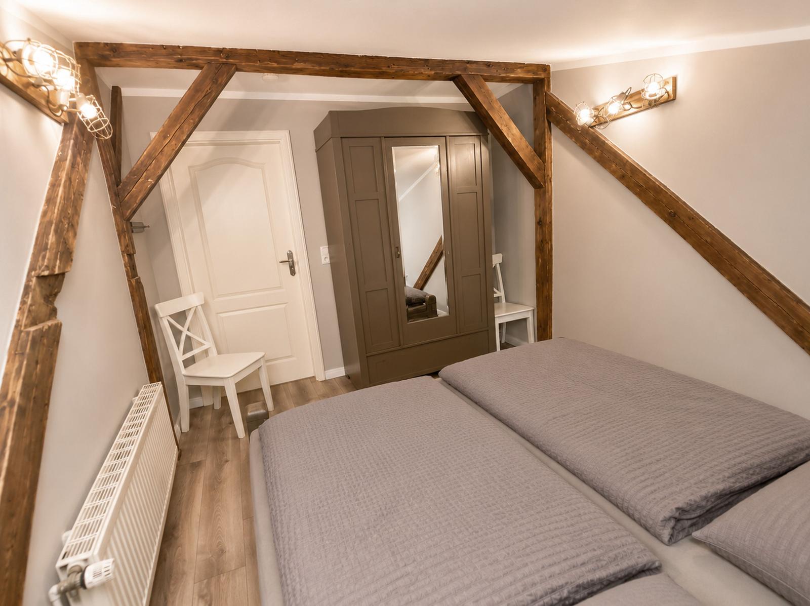 Schlafzimmer mit Holzbalken, Bett, Kleiderschrank und Heizkörper.
