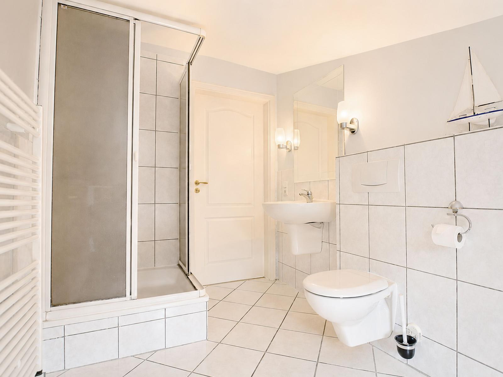 Badezimmer mit Dusche, Toilette und Waschbecken. Wandfliesen und Spiegel sichtbar.