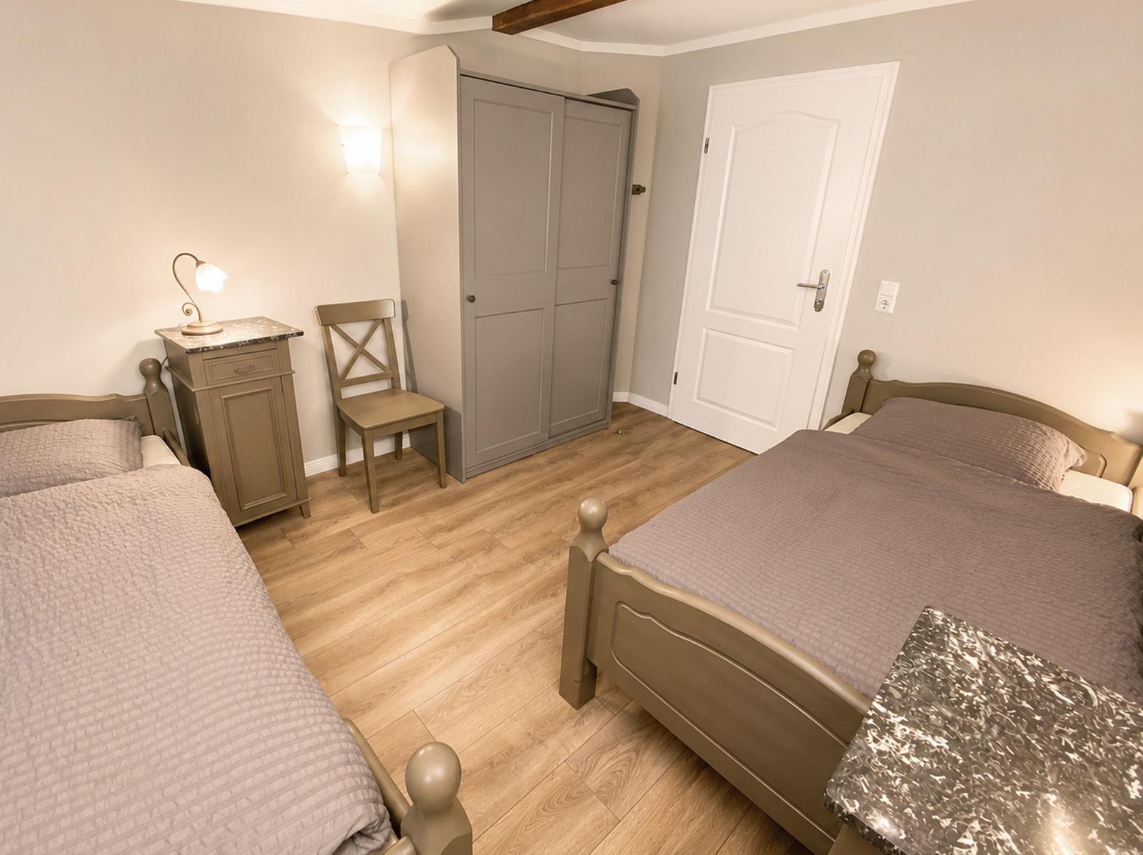 Zwei Betten, Kleiderschrank, Stuhl und Nachttisch in einem Schlafzimmer mit Holzboden.