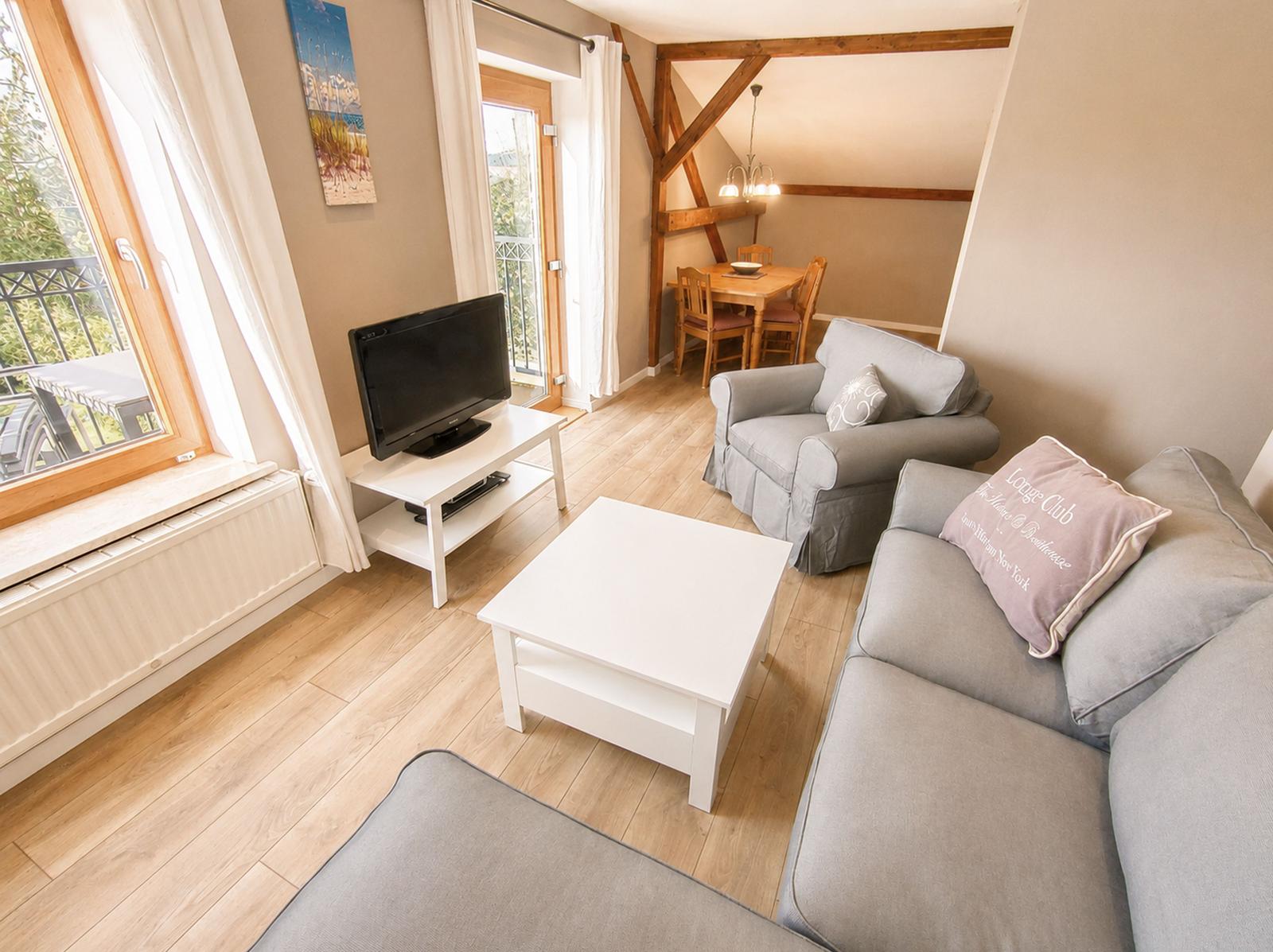 Wohnzimmer mit Sofa, Sessel, Couchtisch und TV. Durchgang zum Essbereich mit Holztisch und Stühlen.