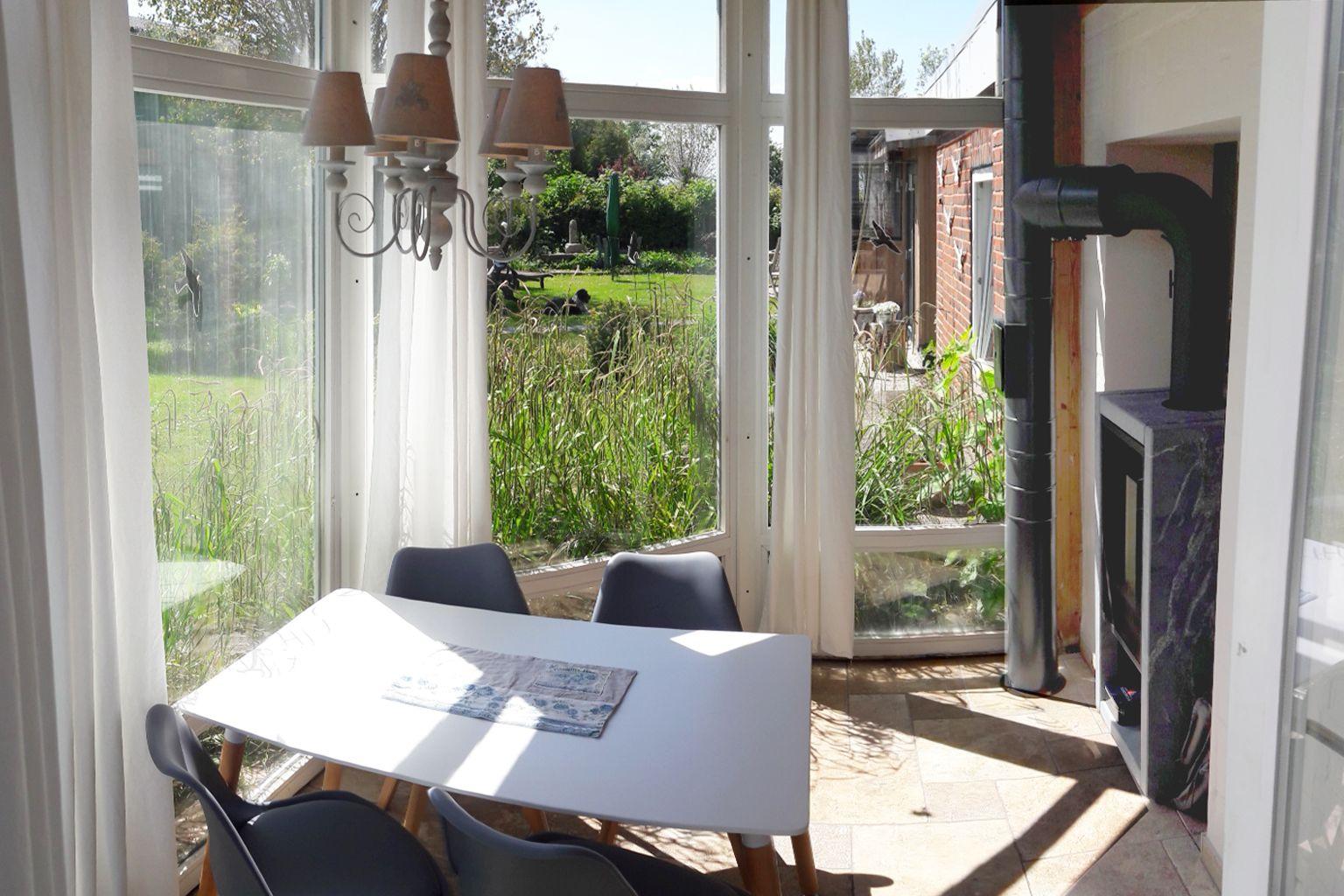 Essbereich mit Tisch und Stühlen, großes Fenster mit Blick auf Garten und Kaminofen.