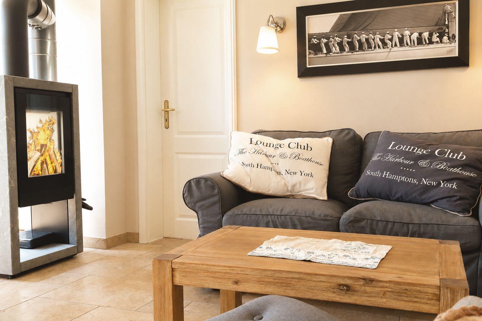 Ein Wohnzimmer mit Sofa, Kamin und Tisch. Auf dem Sofa liegen Kissen mit Aufdruck.