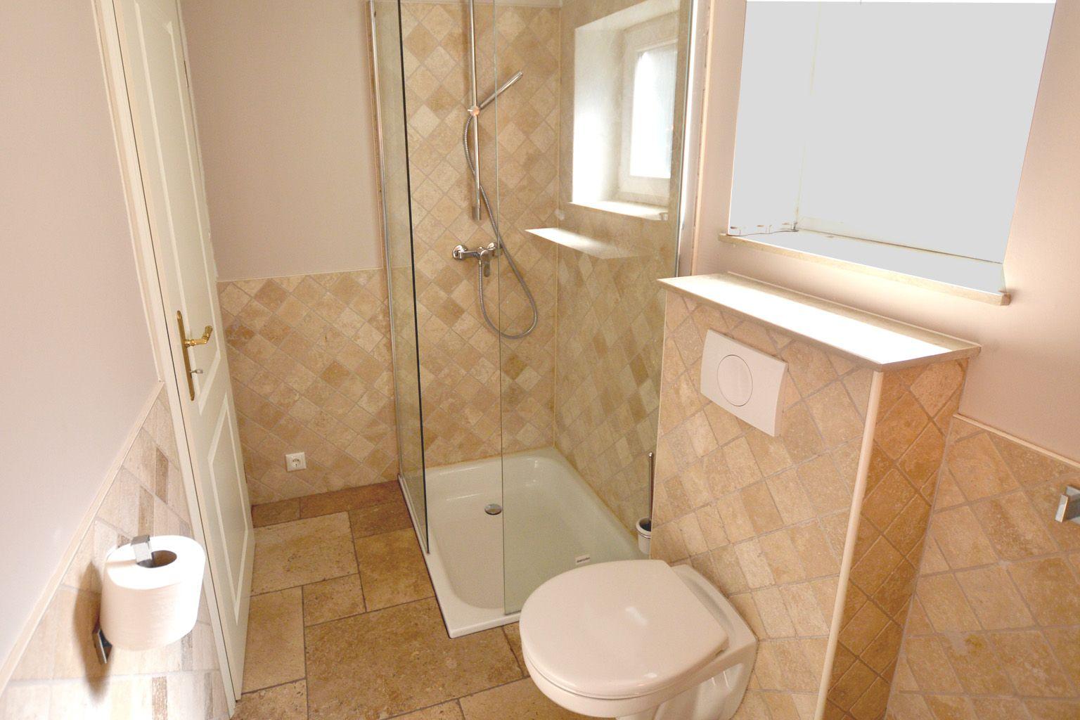 Badezimmer mit Dusche, WC und Spiegel. Fliesenwand und Boden.