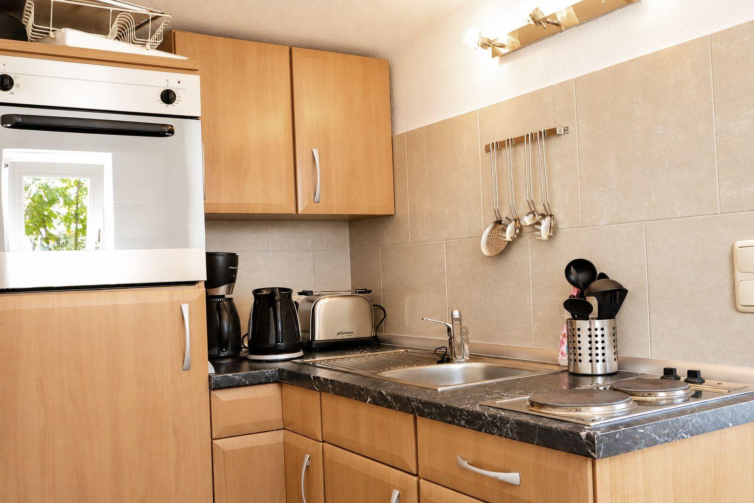 Küche mit Holzschränken, Edelstahlspüle und Kochutensilien an der Wand.