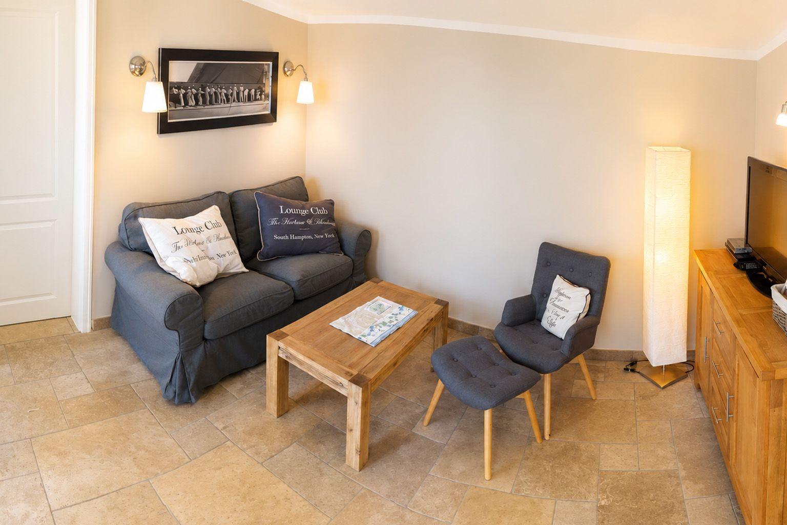 Wohnzimmer mit Sofa, Sessel, Holztisch und Fernseher.
