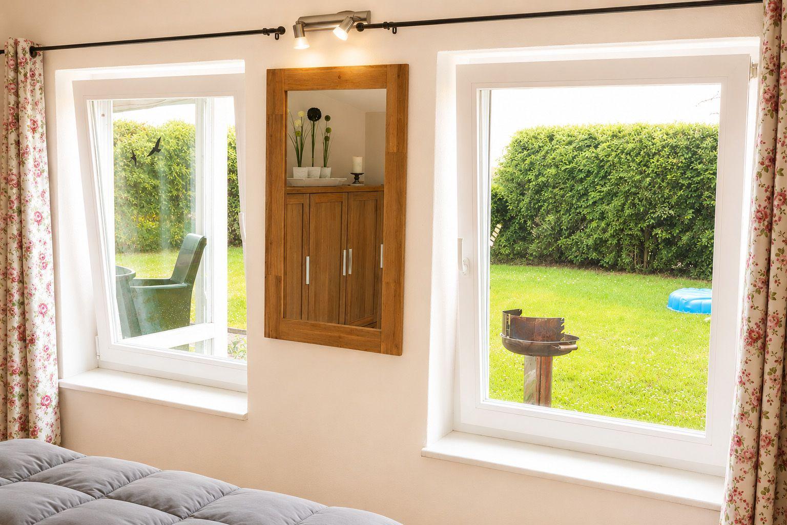 Zimmer mit zwei Fenstern, Spiegelschrank und Blick auf grünen Garten.