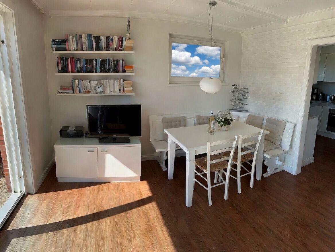 Esszimmer mit Tisch, Stühlen und Fenster. Fernseher und Bücherregale an der Wand.