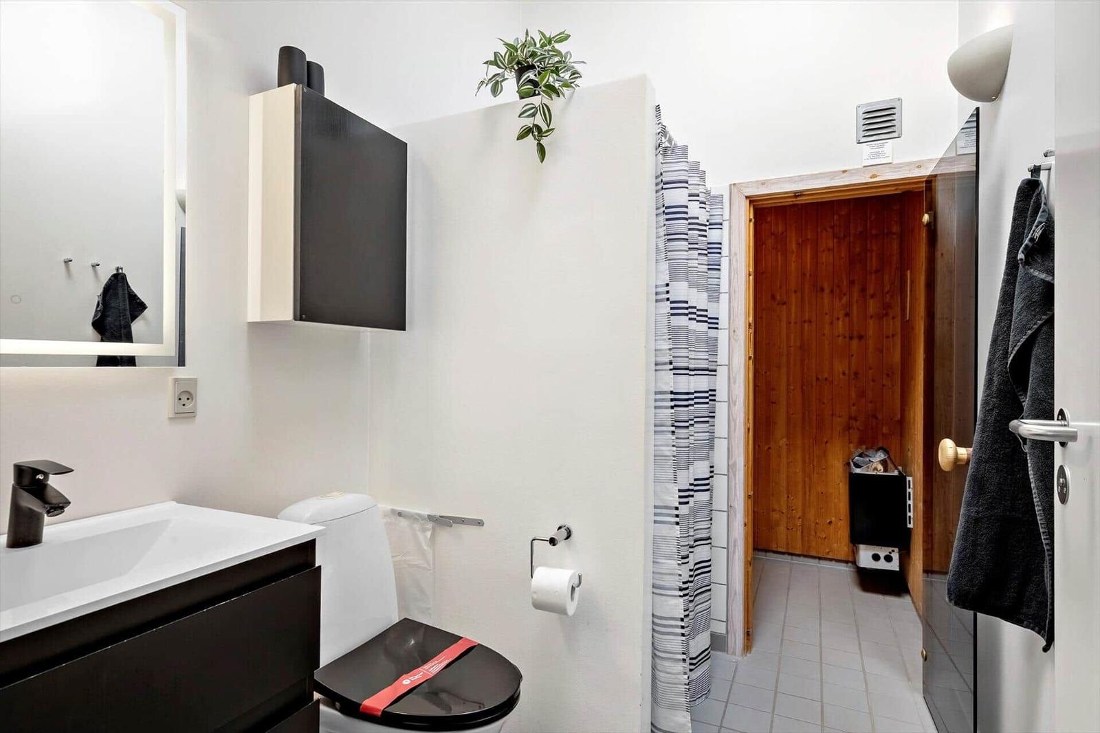 Badezimmer mit Toilette, Waschbecken und Dusche. Sauna im Hintergrund.