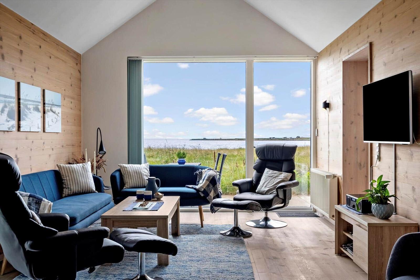 Wohnzimmer mit Blick auf die Landschaft. Holzwände, Sofa, Sessel und Fernseher.