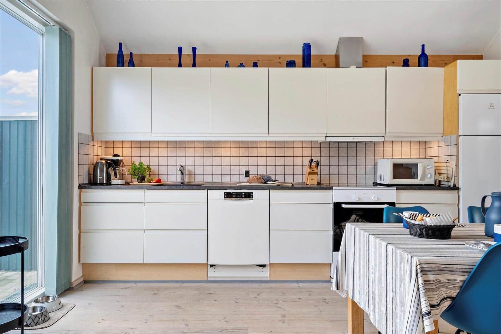 Küche mit weißen Schränken, Arbeitsfläche und Küchengeräten. Tisch mit Tischdecke und Stühlen.