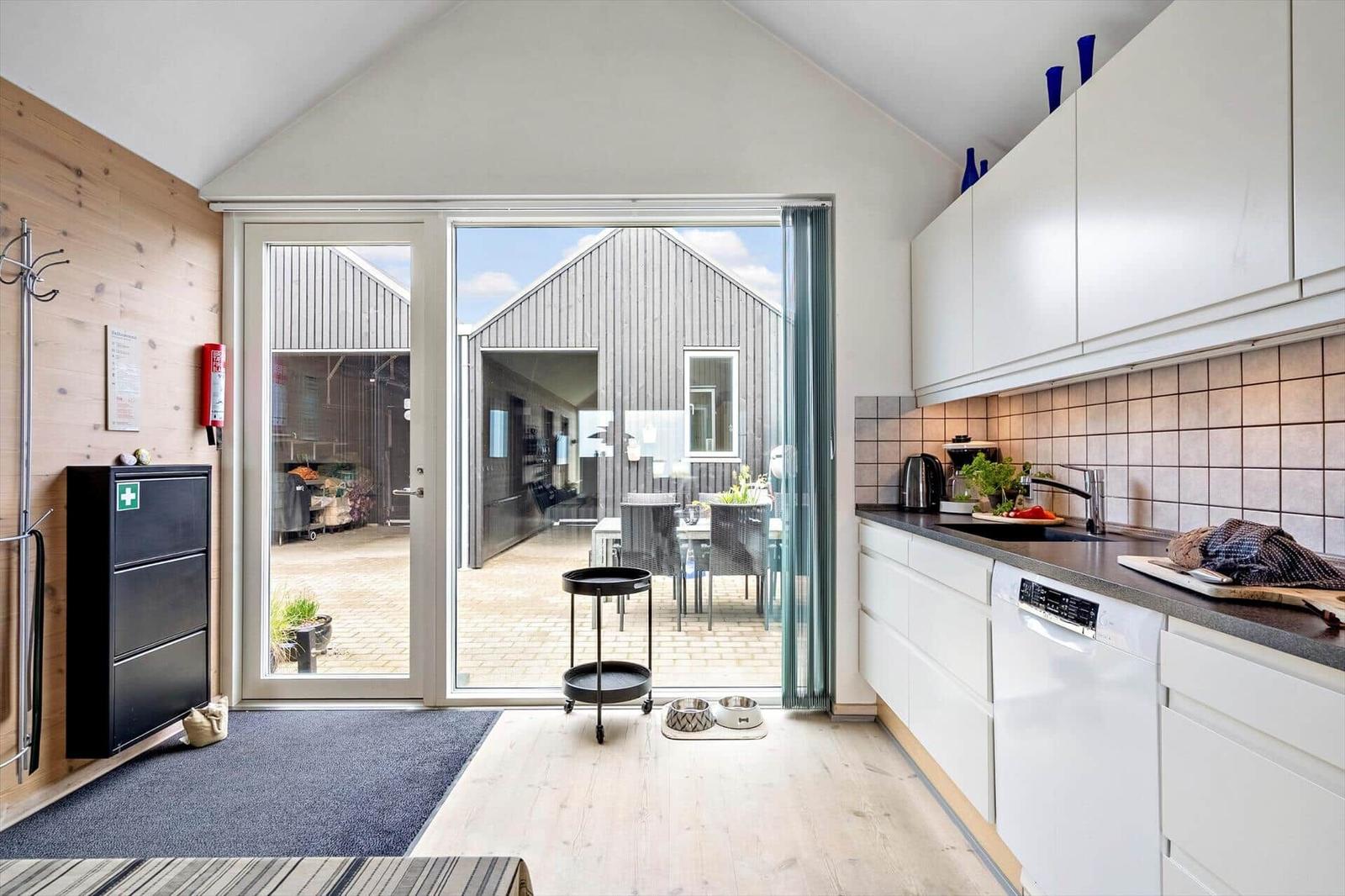 Küche mit Blick auf Terrasse und Gartenhaus. Weiße Schränke, Arbeitsplatte und Spüle.
