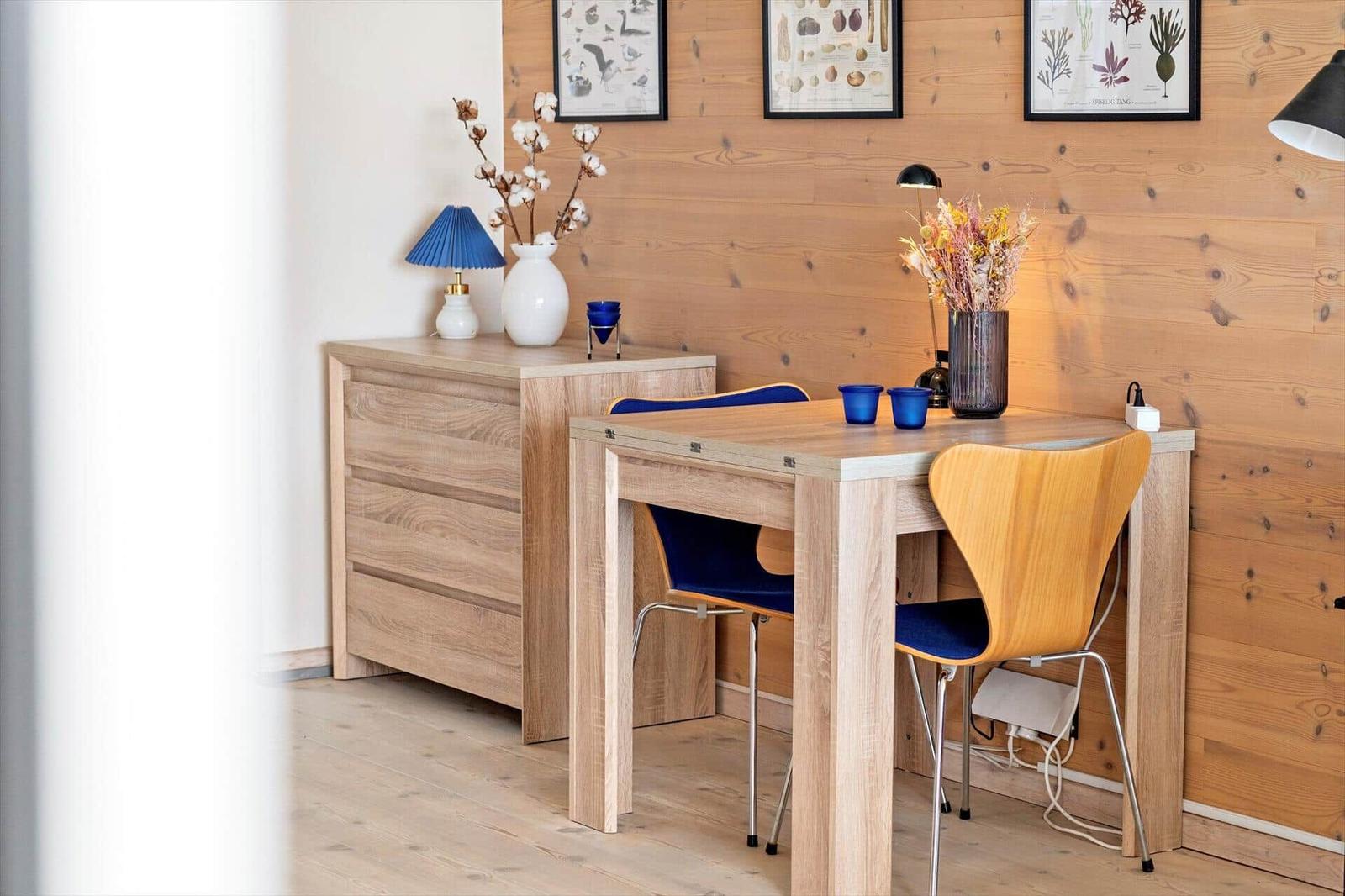 Holztisch mit zwei Stühlen, Schrank und Wanddekoration in einem Raum mit Holzwand.