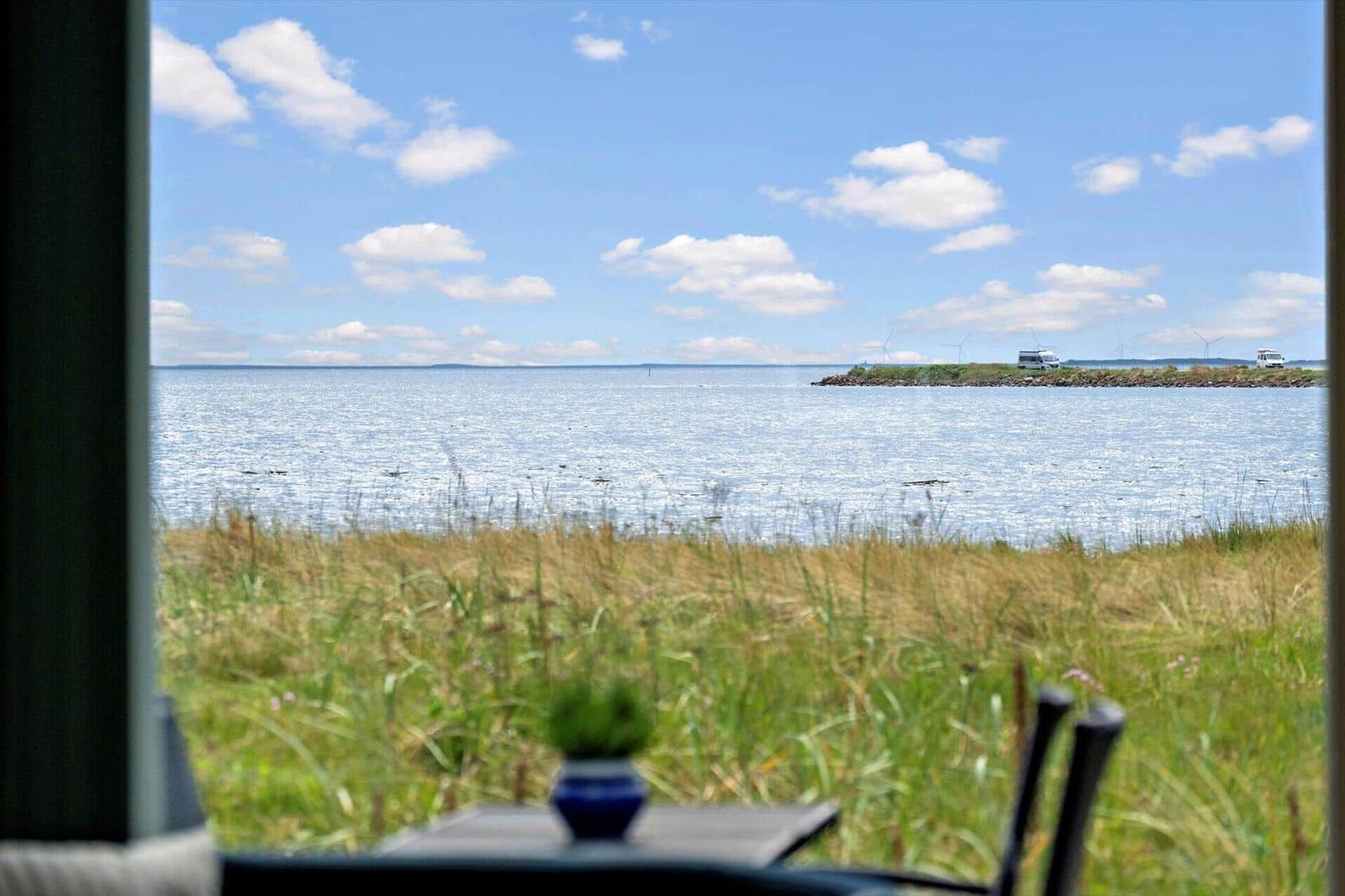 Aus dem Fenster blickt man auf eine ruhige Wasserfläche mit Grasland und zwei Wohnmobilen in der Ferne.
