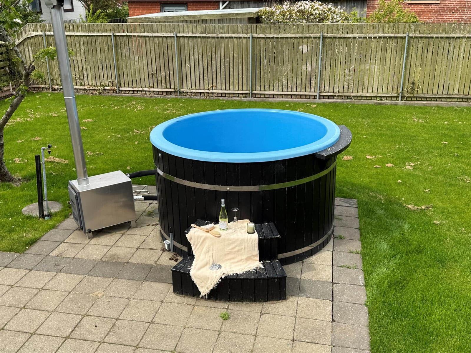 Ein schwarzer Whirlpool mit blauem Innenbereich steht auf einer Terrasse mit Grünfläche.