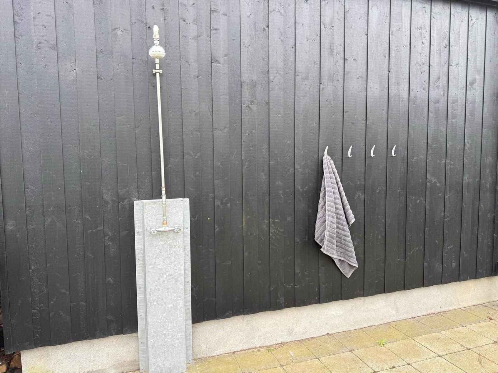 Außen-Dusche mit Duschbrause und Wandhalterung an dunklem Holzzaun.