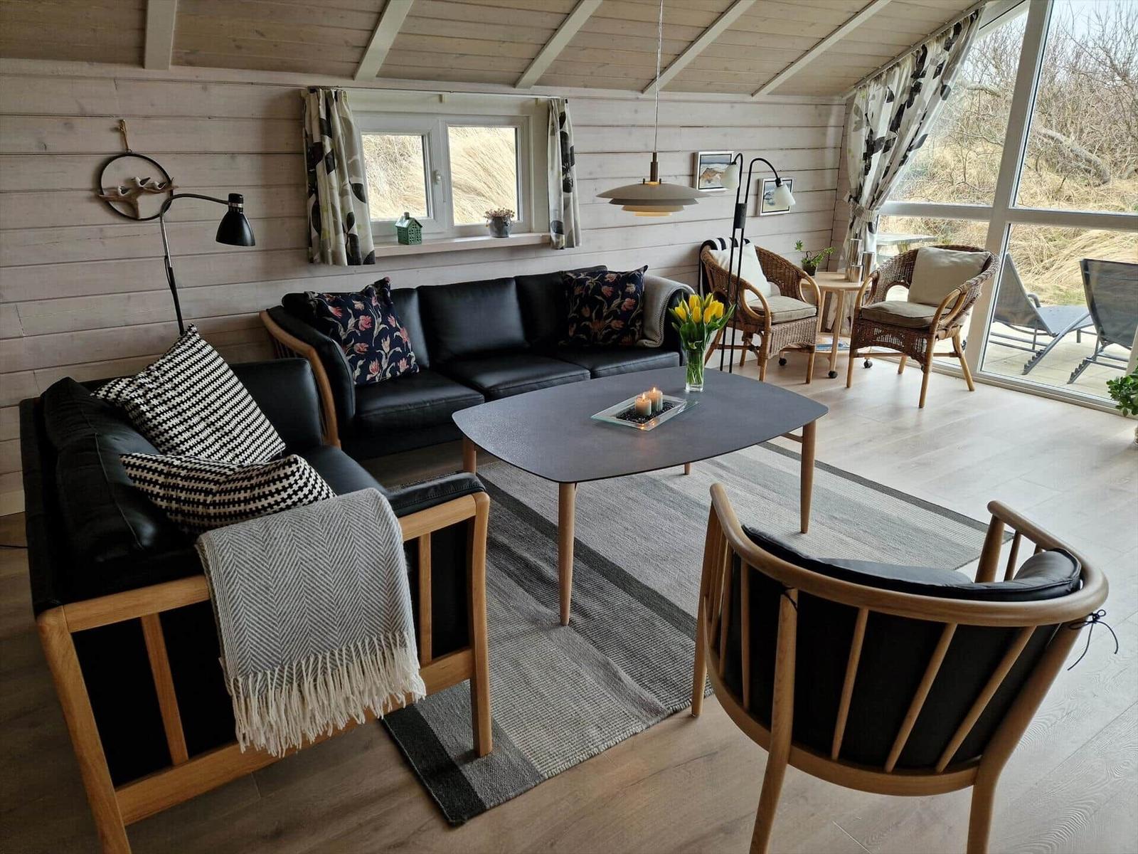 Wohnzimmer mit Sofa, Stühlen und Tisch. Durchgang zur Terrasse mit Sitzgelegenheiten.