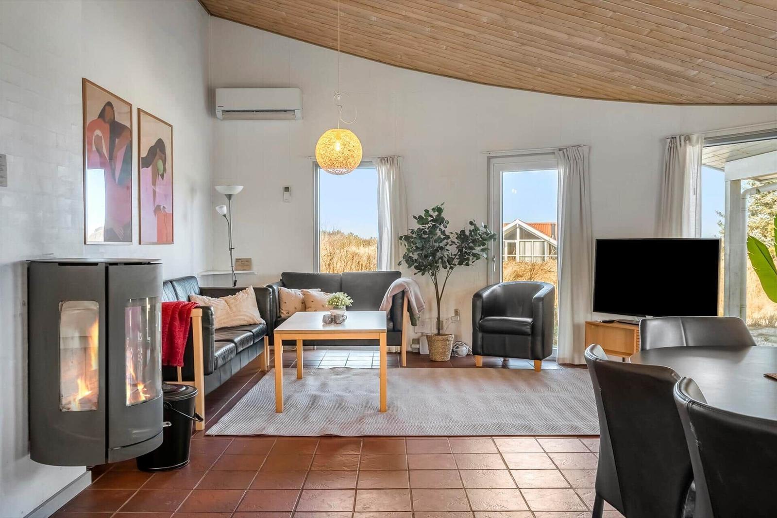 Wohnzimmer mit Kamin, Sofa, Esstisch und Blick auf Außenbereich.