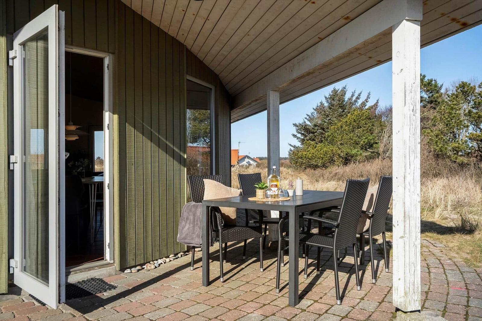 Terrasse mit Tisch und Stühlen, Zugang zum Haus durch Glastür.