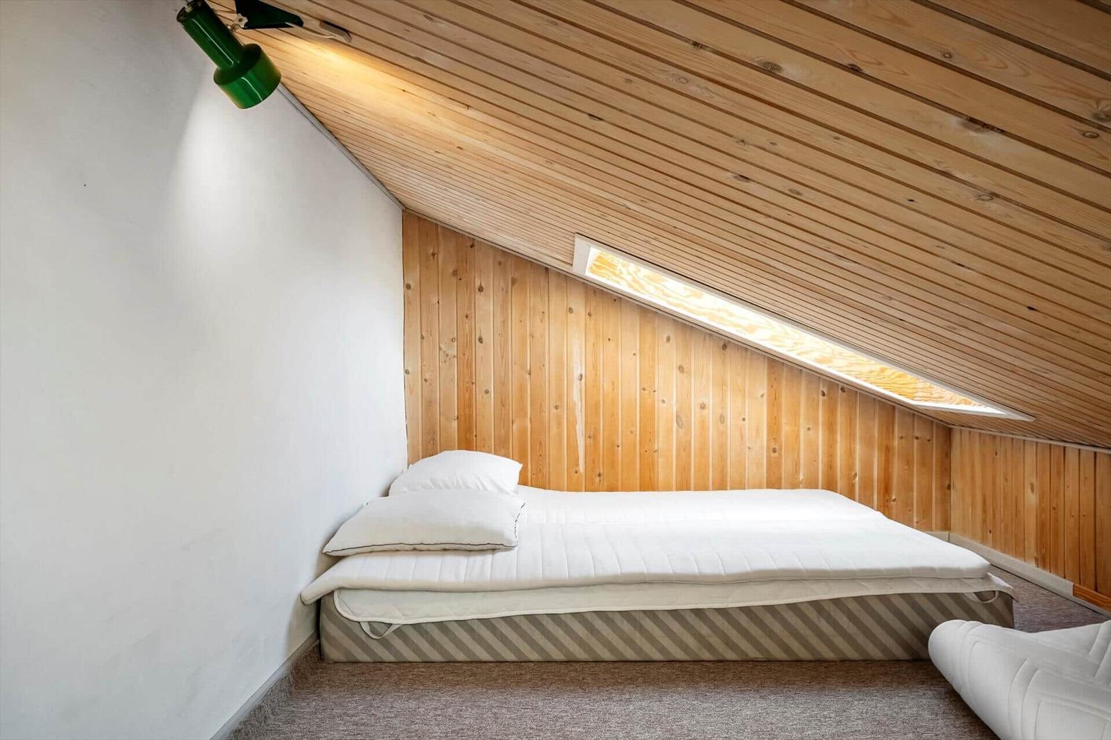Schlafzimmer mit Dachschräge, Holzwand und Bett unter Dach