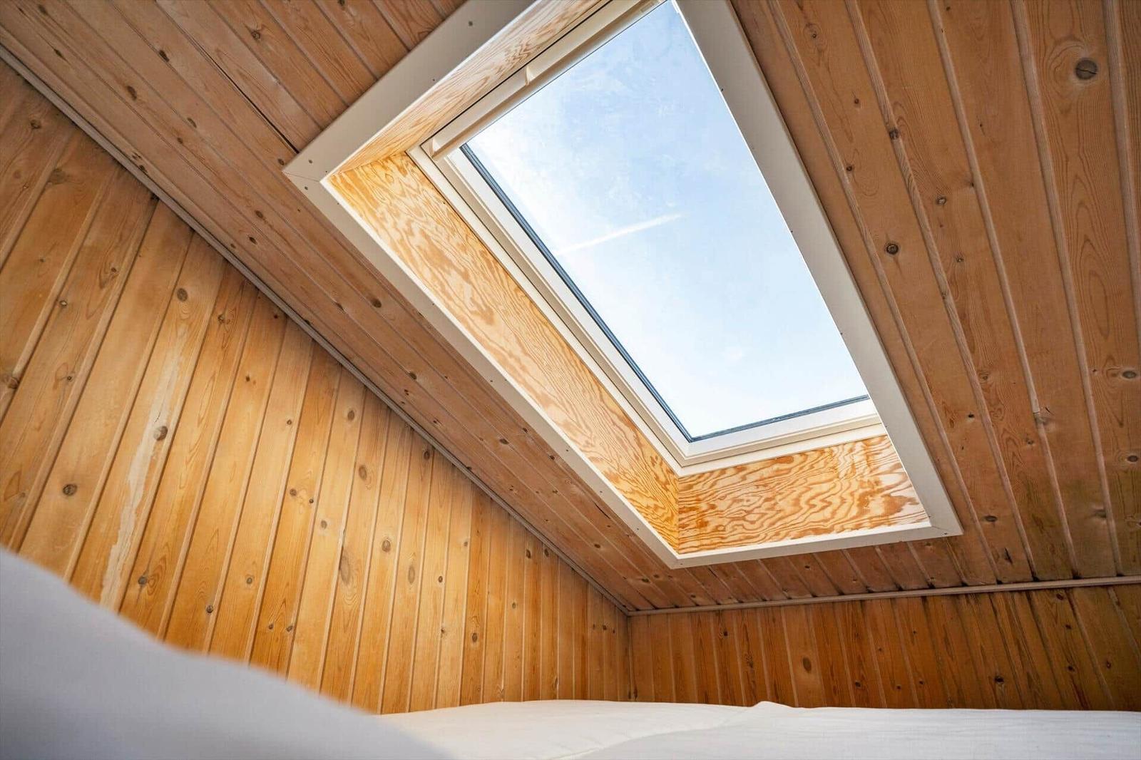 Dachgeschosszimmer mit Holzwand und Dachfenster. Blick auf den Himmel.