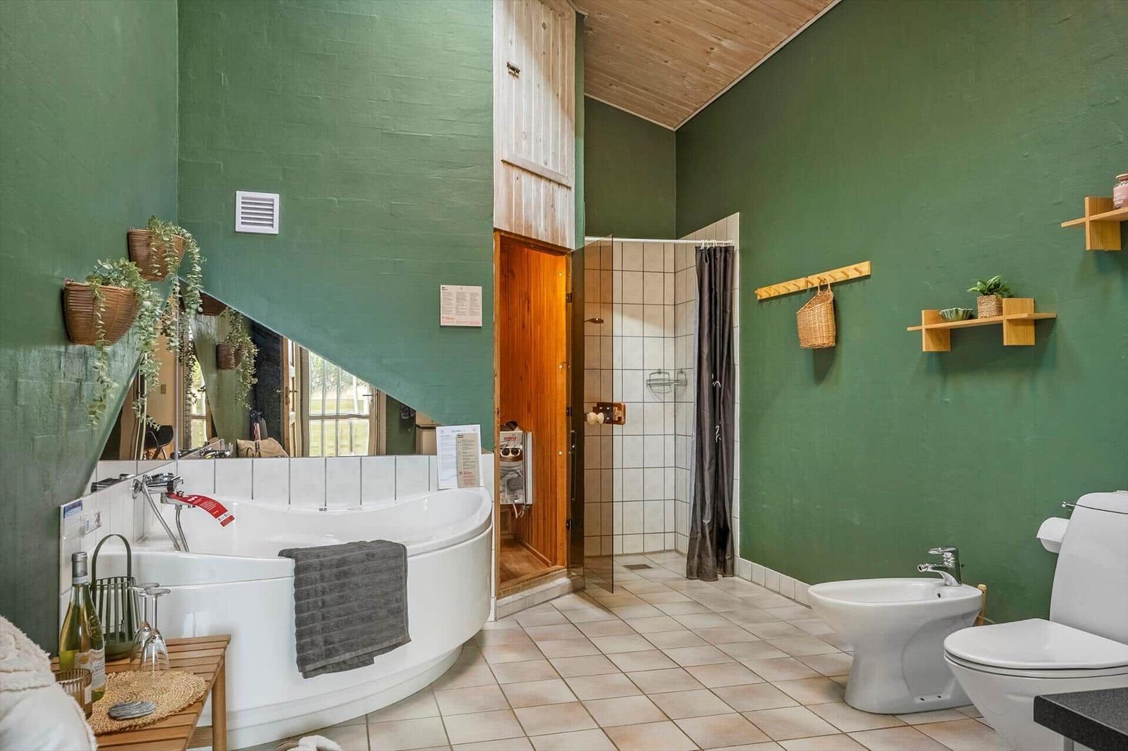 Badezimmer mit Badewanne, Dusche, WC und Holzregalen an grünen Wänden.