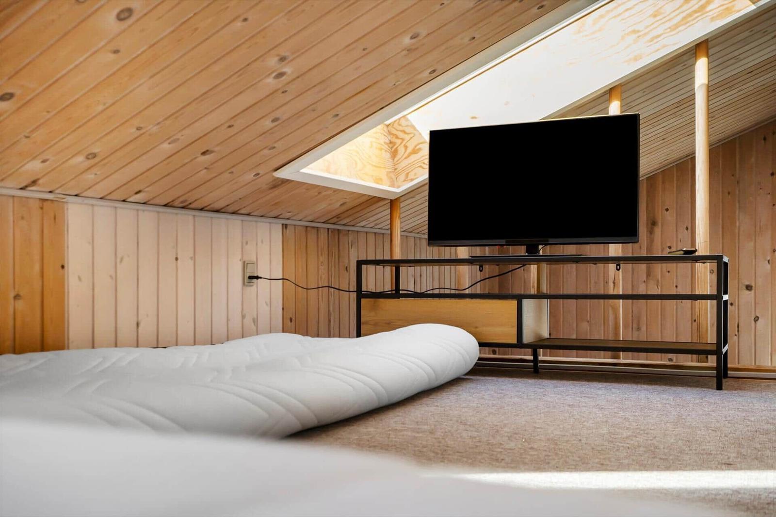 Schlafzimmer mit Matratze, Fernseher und Holzwand