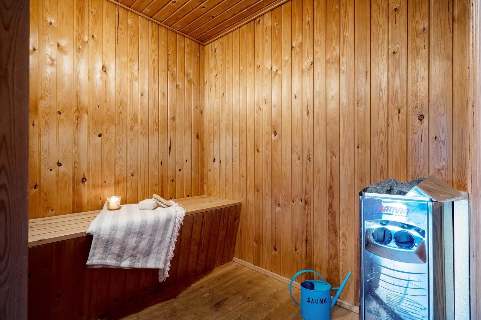 Sauna mit Holzwand, Sitzbank, Deckenventilator und blauem Eimer.