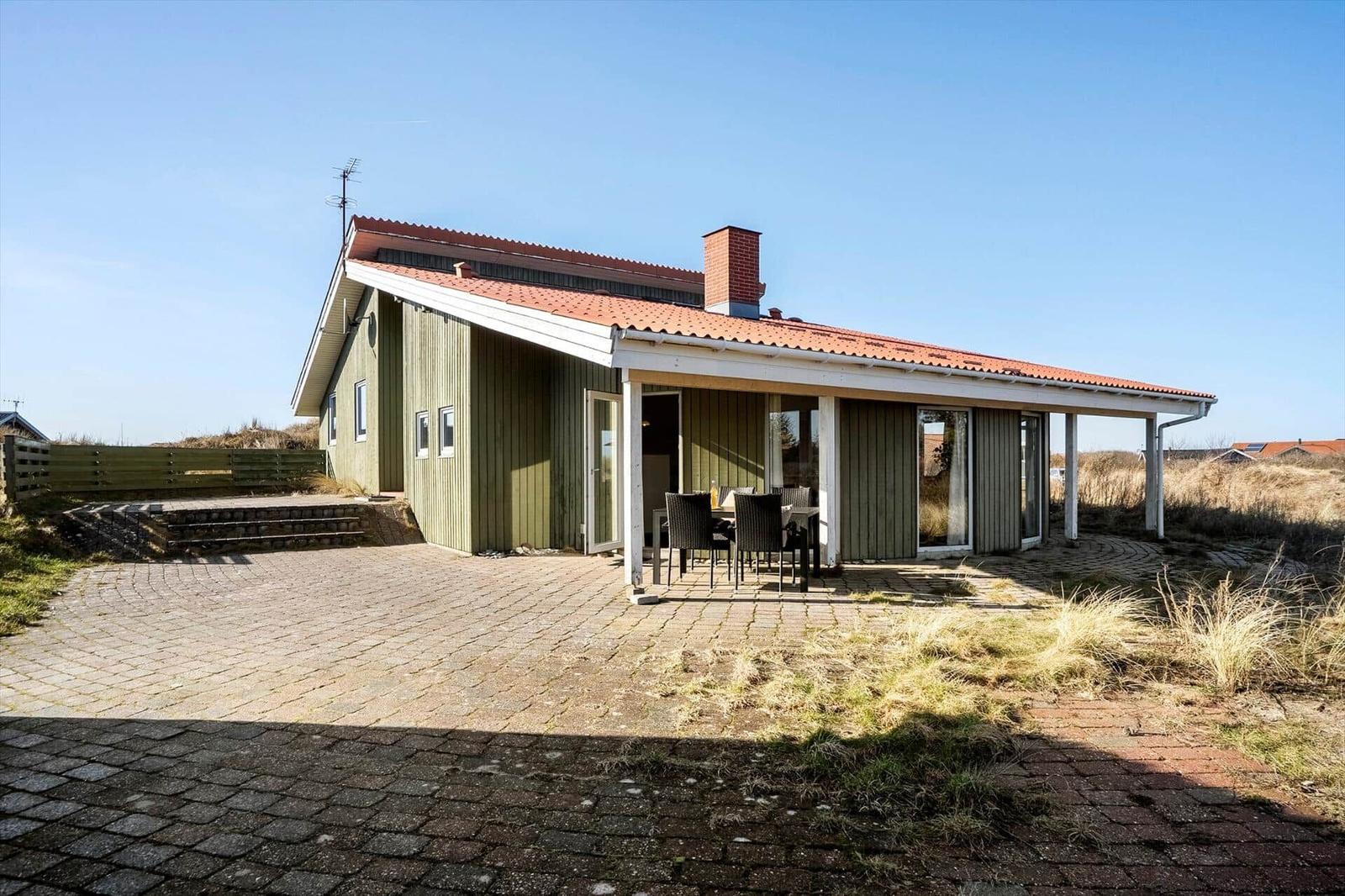 Holzhaus mit Terrasse und Grillplatz. Außenbereich mit Tisch und Stühlen. Kiesweg und Grasfläche.