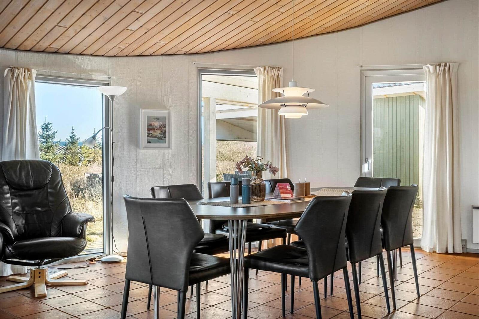 Essbereich mit runder Tisch und sechs Stühlen, Holzdecke und Fenster zur Aussicht.