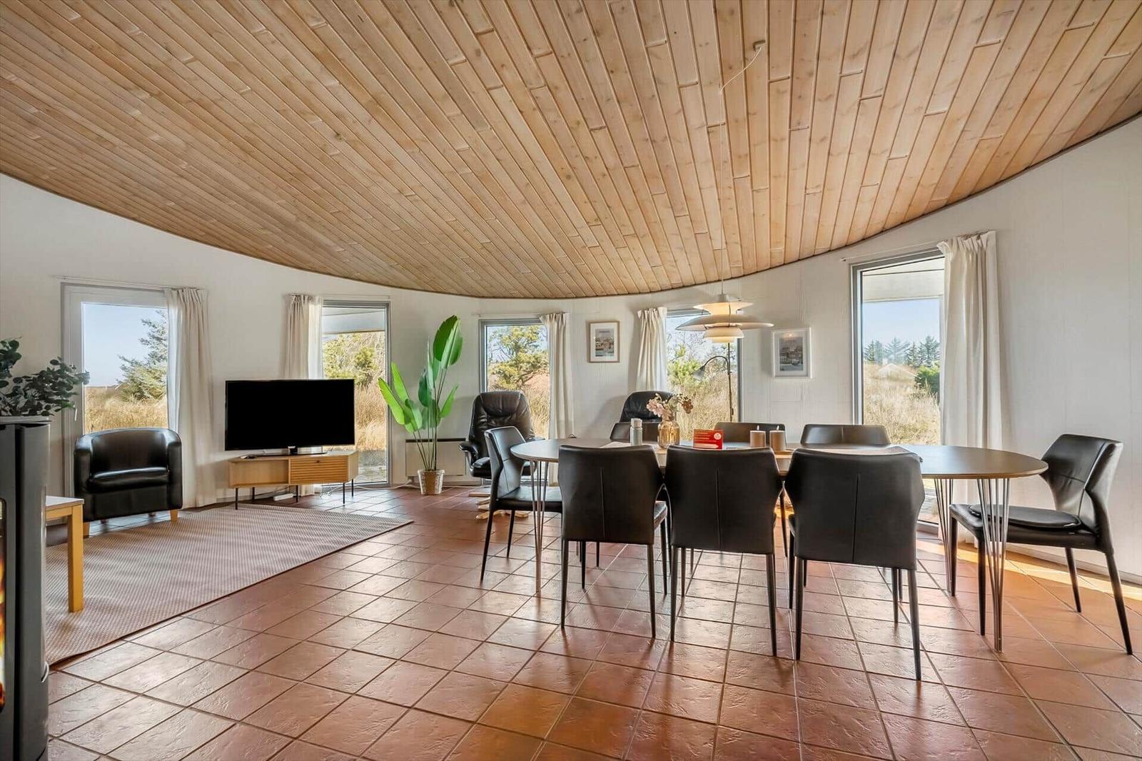 Rundes Wohn- und Esszimmer mit Holzdecke, Terrakottaboden und großen Fenstern.