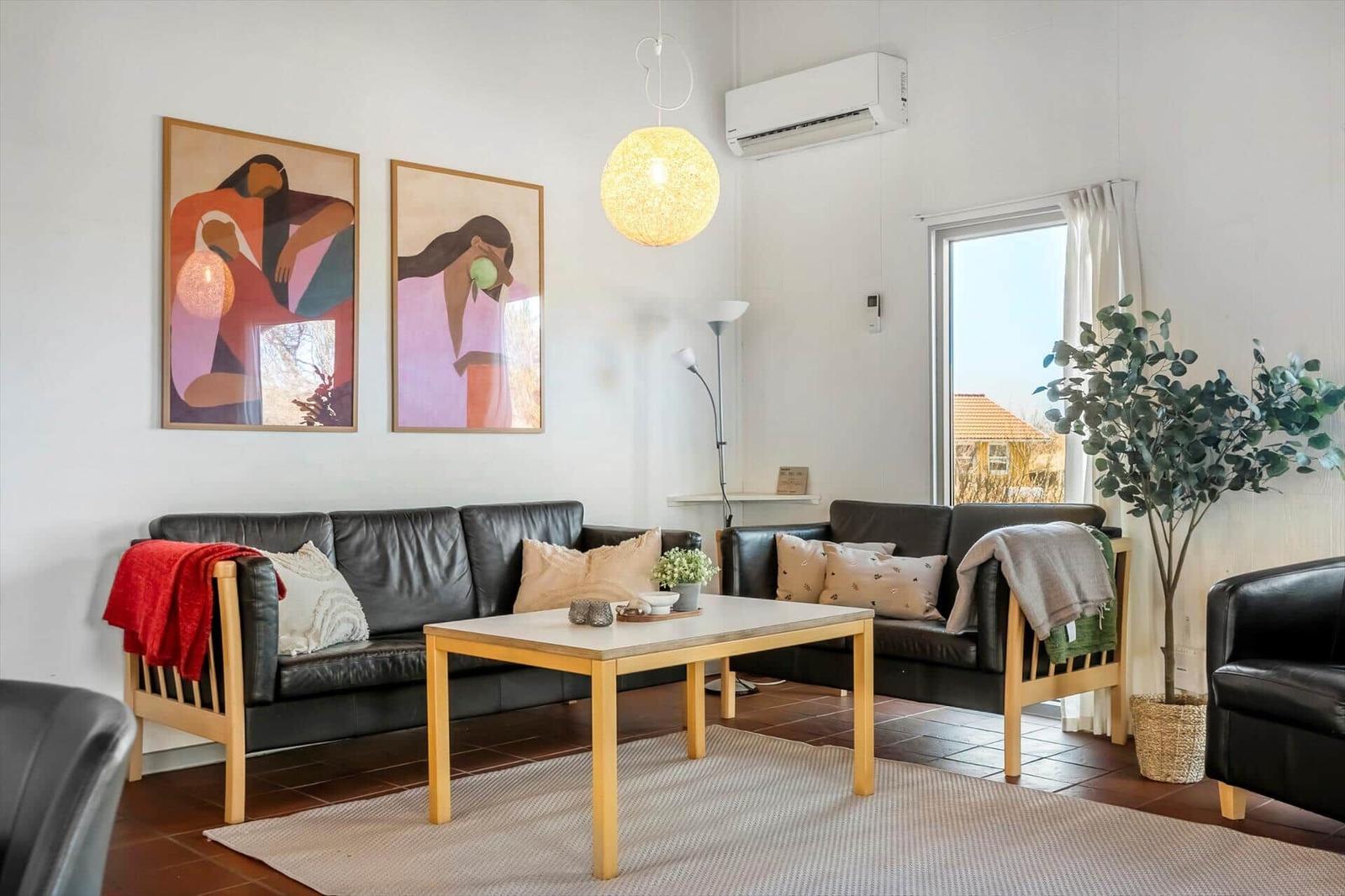Wohnzimmer mit zwei schwarzen Sofas, Tisch und Wandbildern.