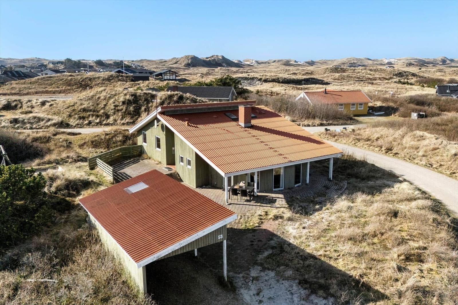 Ein Haus mit rotem Dach und Holzverkleidung liegt in einer Dünenlandschaft.