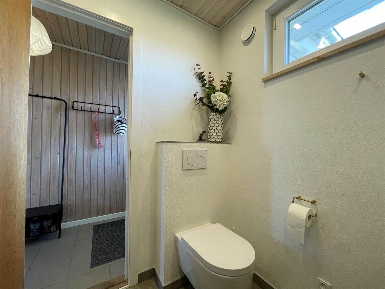 Toilette mit Blumenvase und Fenster. Durchgang zu einem Raum mit Holzwand.