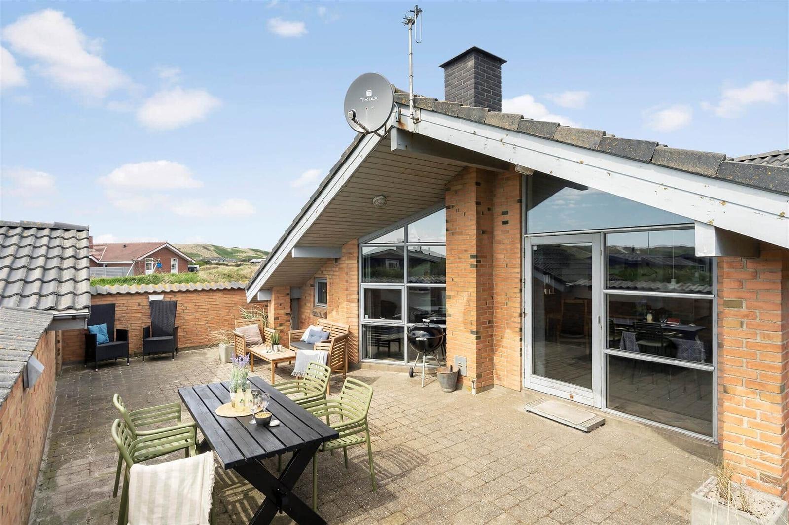 Terrasse mit Sitzgelegenheiten und Grillplatz. Glasfront führt ins Haus. Dach mit Satellitenschüssel.