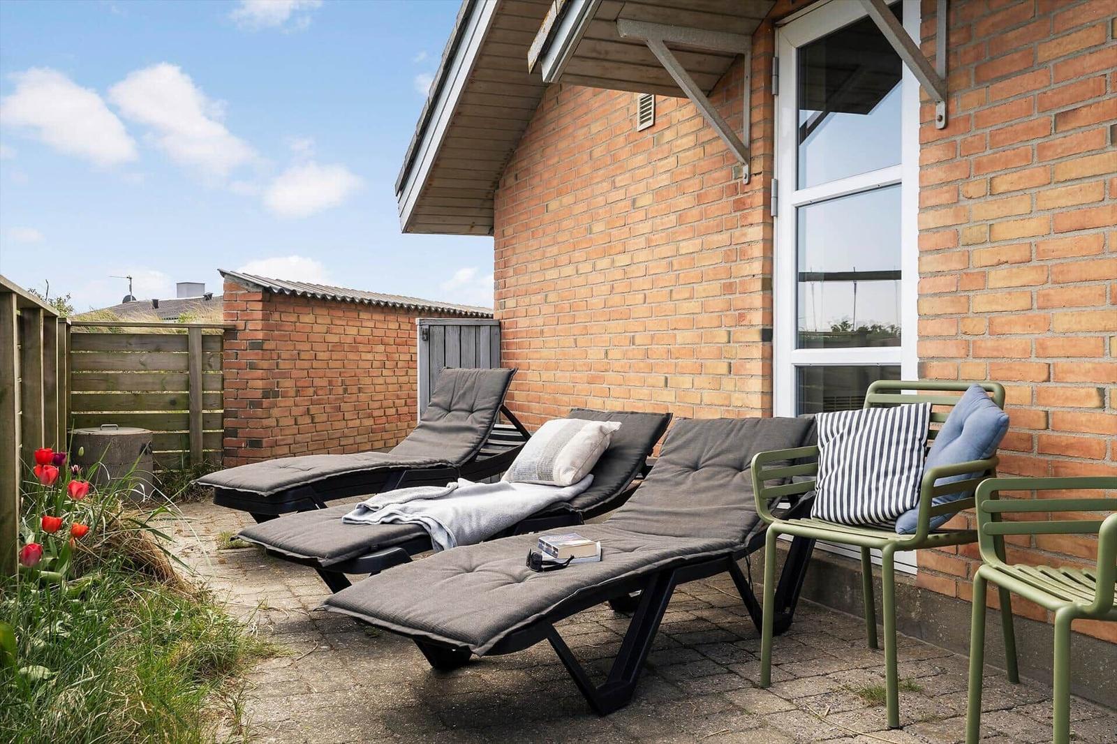 Terrasse mit Liegen, Stühlen und Tulpen vor Backsteinhaus