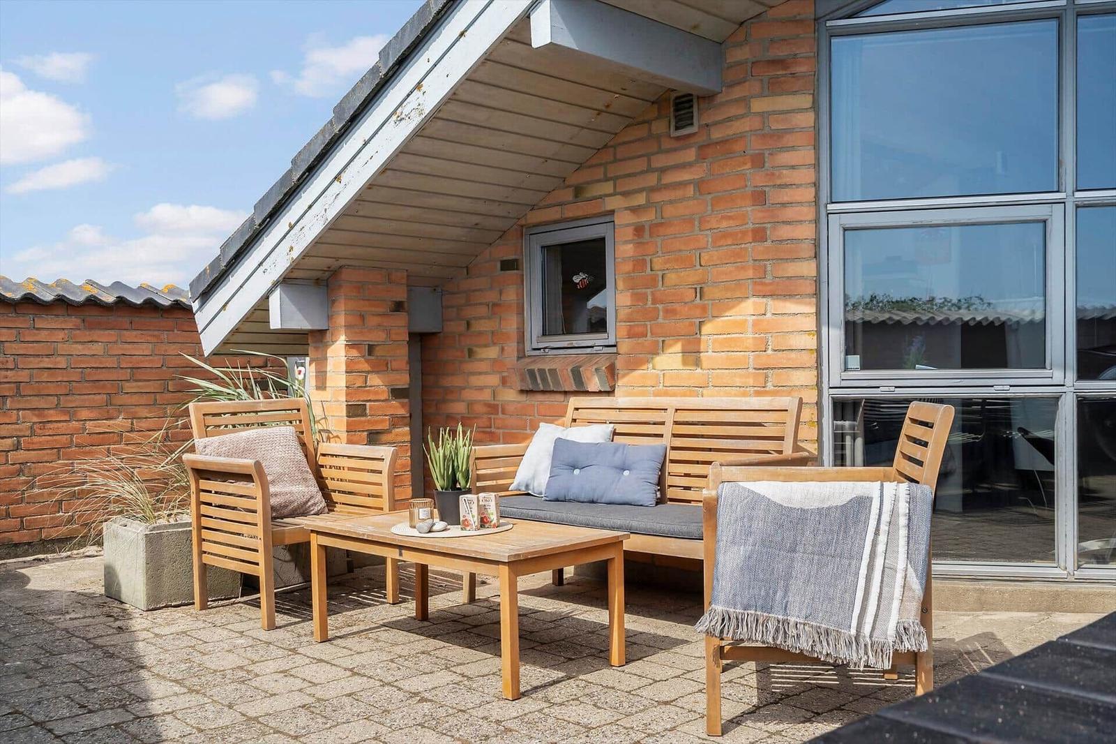 Terrasse mit Holzmöbeln, Sitzbank und Tisch vor Backsteinhaus mit Glasfassade.